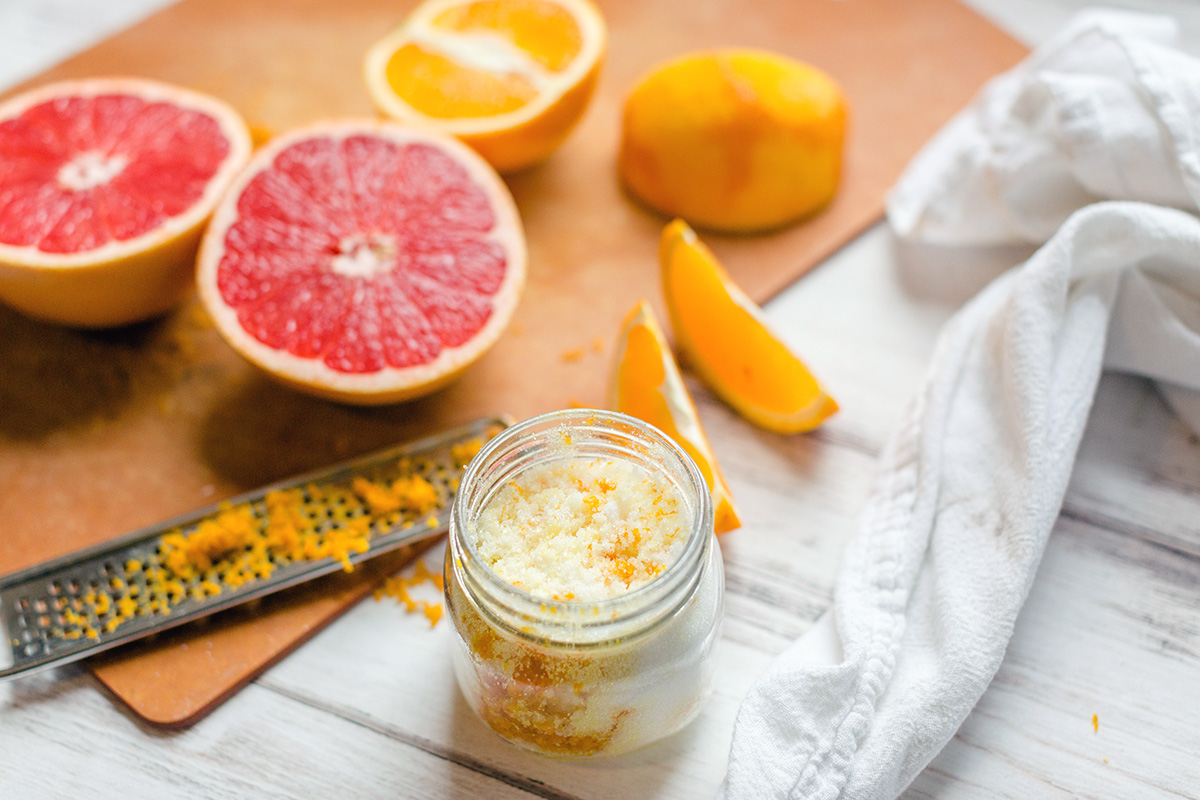 A grapefruit cut in half on a cutting board next to a zested orange and a jar of orange sugar