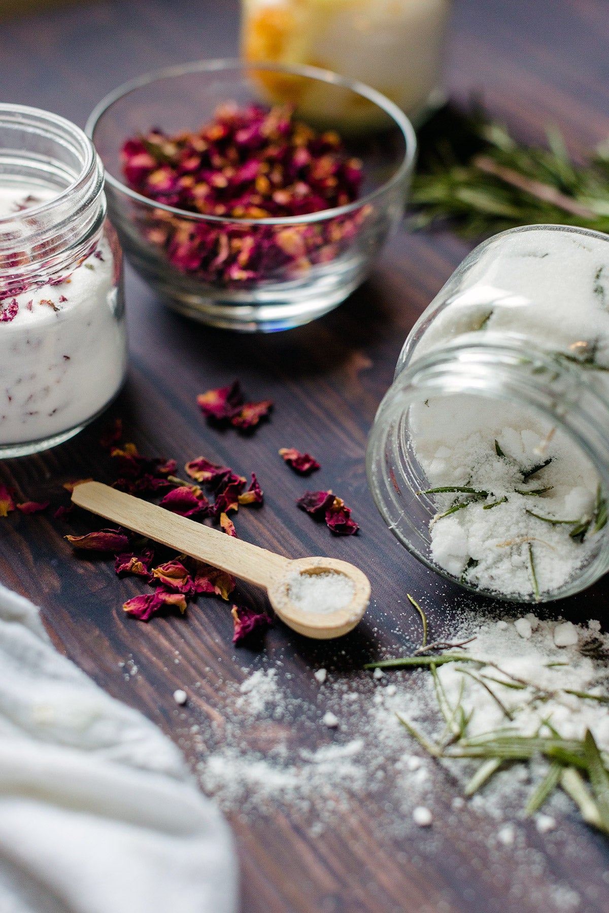 A container of rosemary sugar spilling out onto a kitchen table with rose sugar in the background