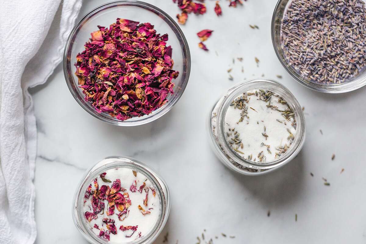 A jar of sugar next to a pile of rose petals and lavendar, ready to be infused