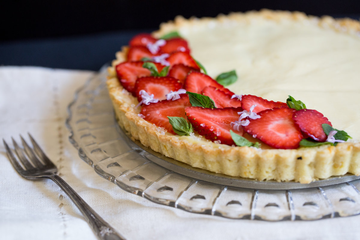 A tart filled with basil-infused pastry cream and decorated with strawberries and edible flowers