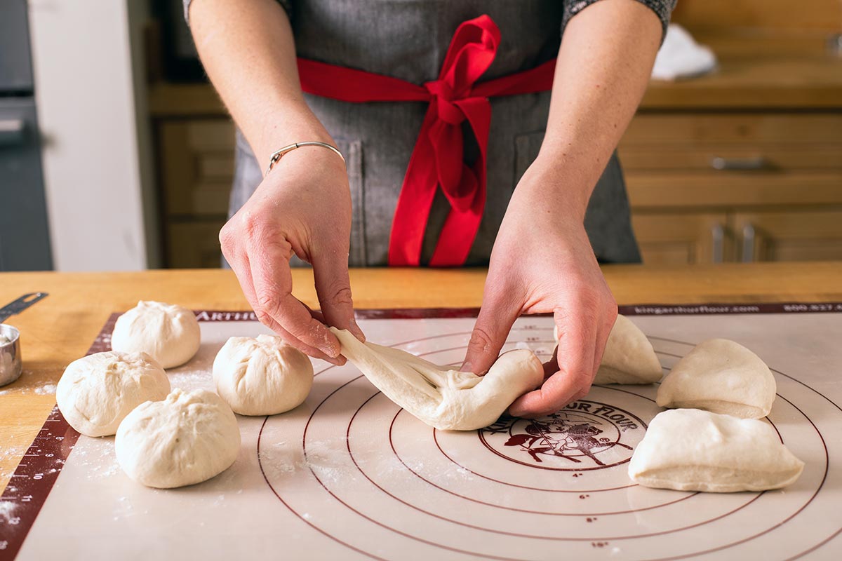 A baker preshaping bagel dough into little dumplings in preparation for final shaping