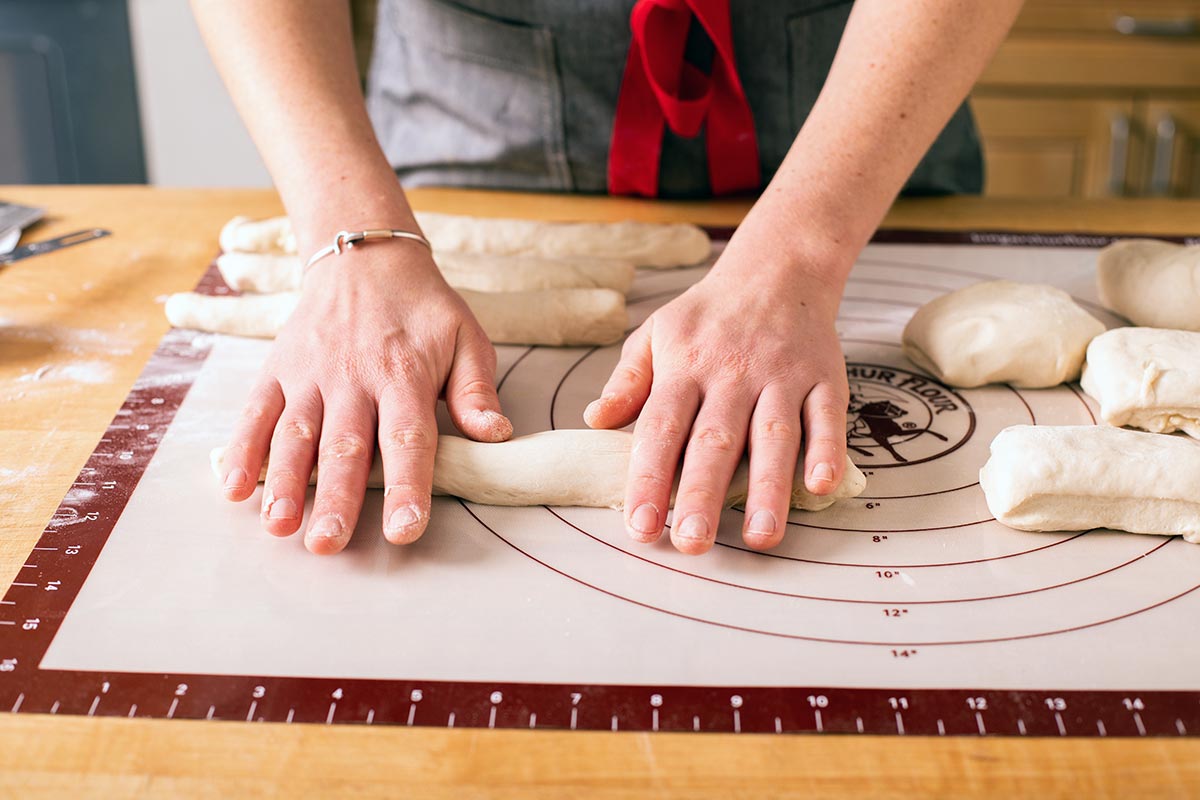 A baker preshaping bagel dough into wide logs