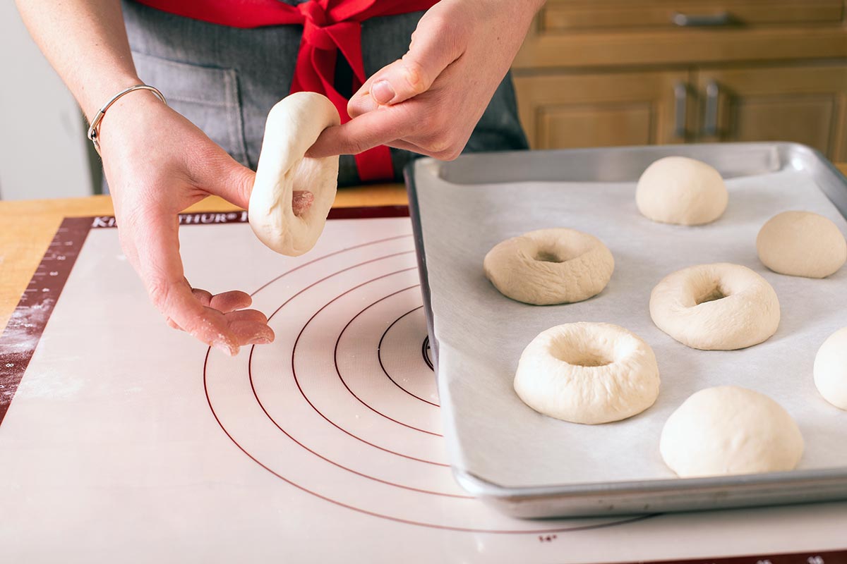 A baker twirling a bagel round their fingers, enlarging the center hole so that it’s about 2” in diameter