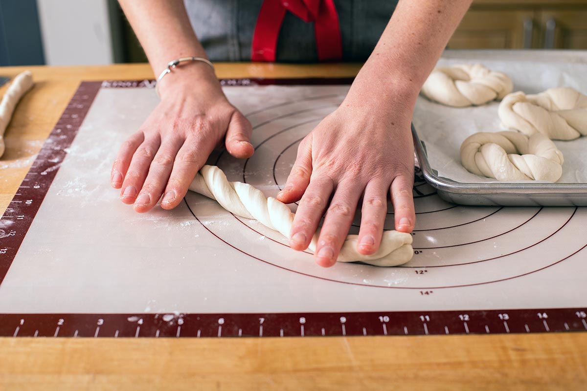 A baker’s hands poised on the ends of two strands of dough, twisting them together