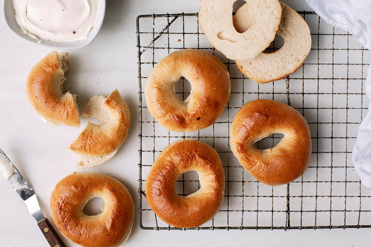 Freshly baked plain bagels on a cooling rack with some sliced in half