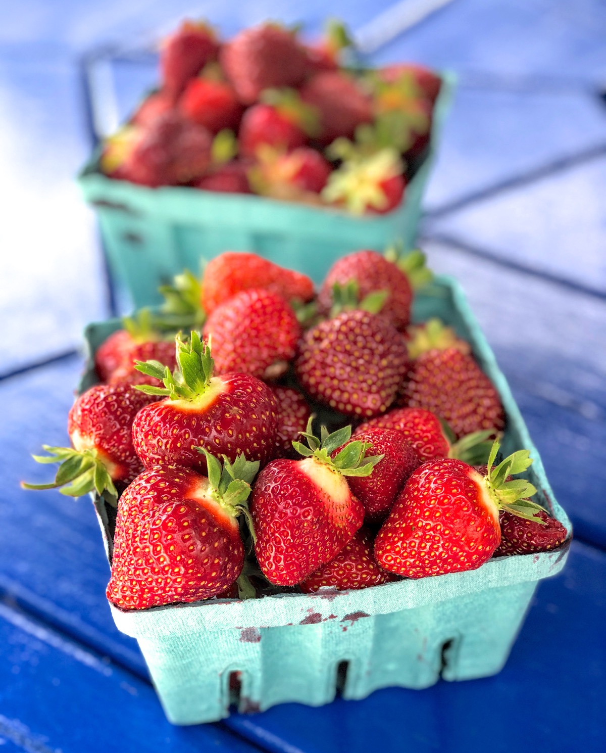 Two quart baskets of fresh-picked strawberries set on a blue table.