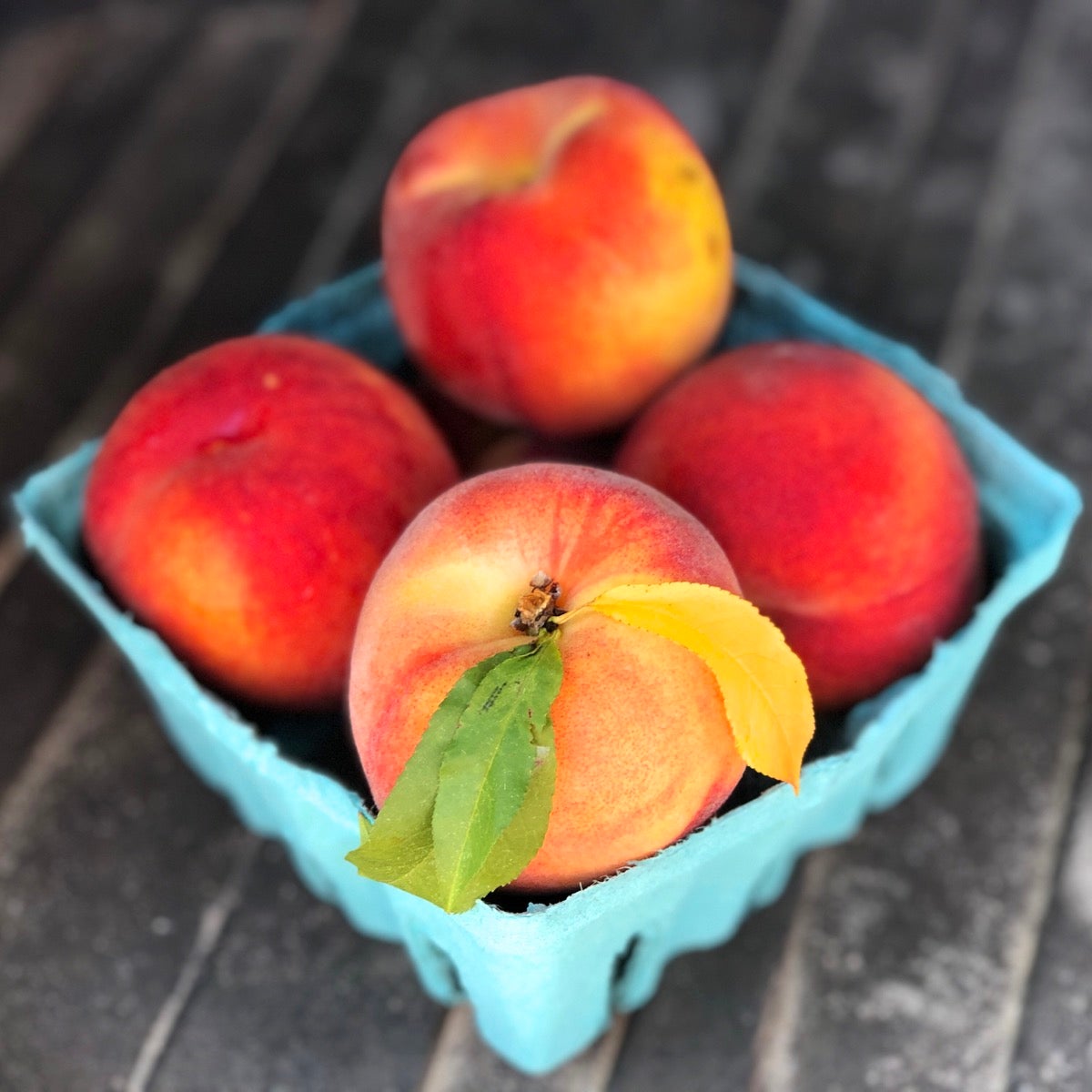 A quart jar of beautiful fresh peaches, one with leaves intact.