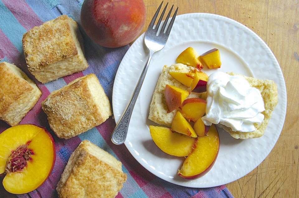 Almond Flour Shortcakes, one split on a plate with sliced peaches and whipped cream.