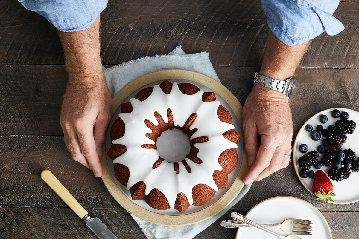 A baker presenting a Bundt cake topped with glaze