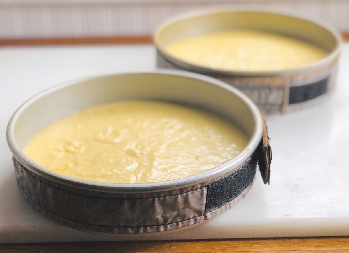 Two batches of cake batter in round cake pans encircled with cake strips, ready to bake.