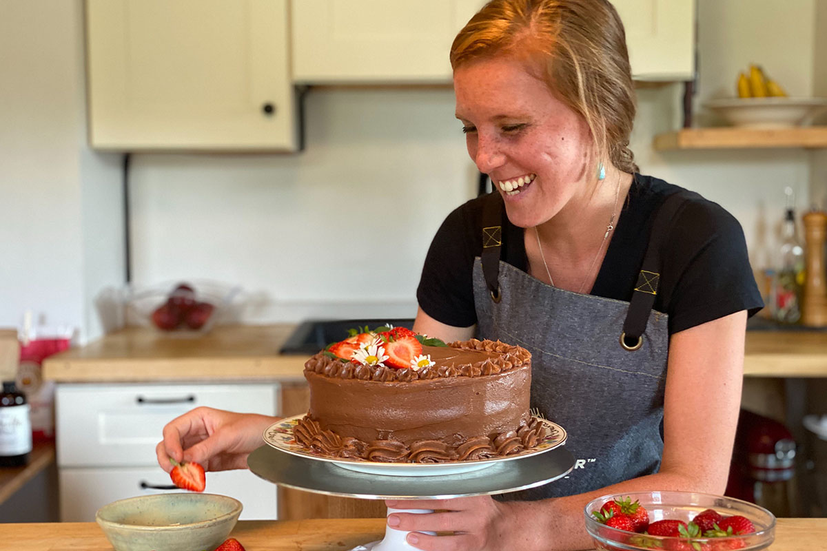 A baker decorating a chocolate layer cake