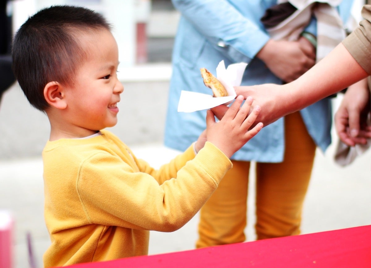 Little boy being handed a slice of pizza.