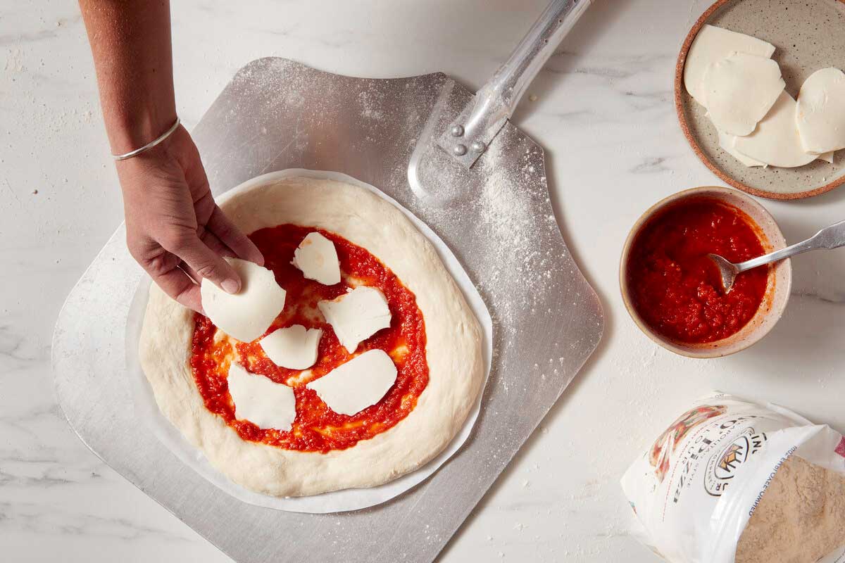 Sauced pizza being topped with cheese