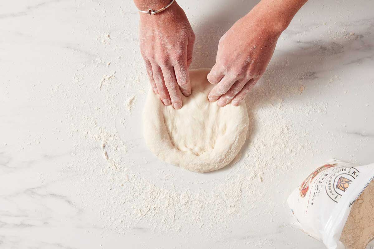 Fingers pressing pizza dough into a circle, with outer edge intact