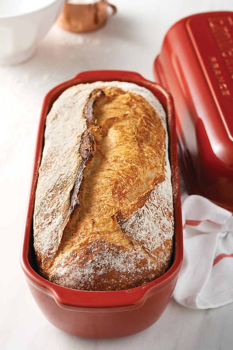 A loaf of sourdough bread in a ceramic loaf pan