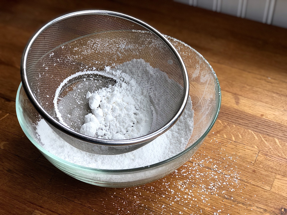 Confectioners' sugar sifted through a sieve into a bowl.
