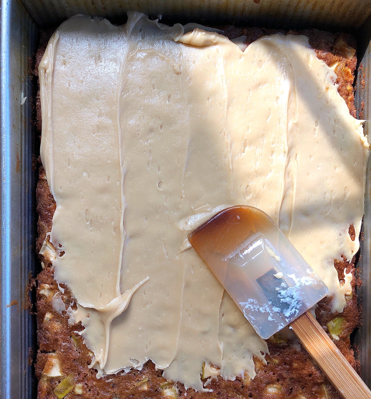 Apple Cake in a rectangular pan being frosted with brown sugar frosting.
