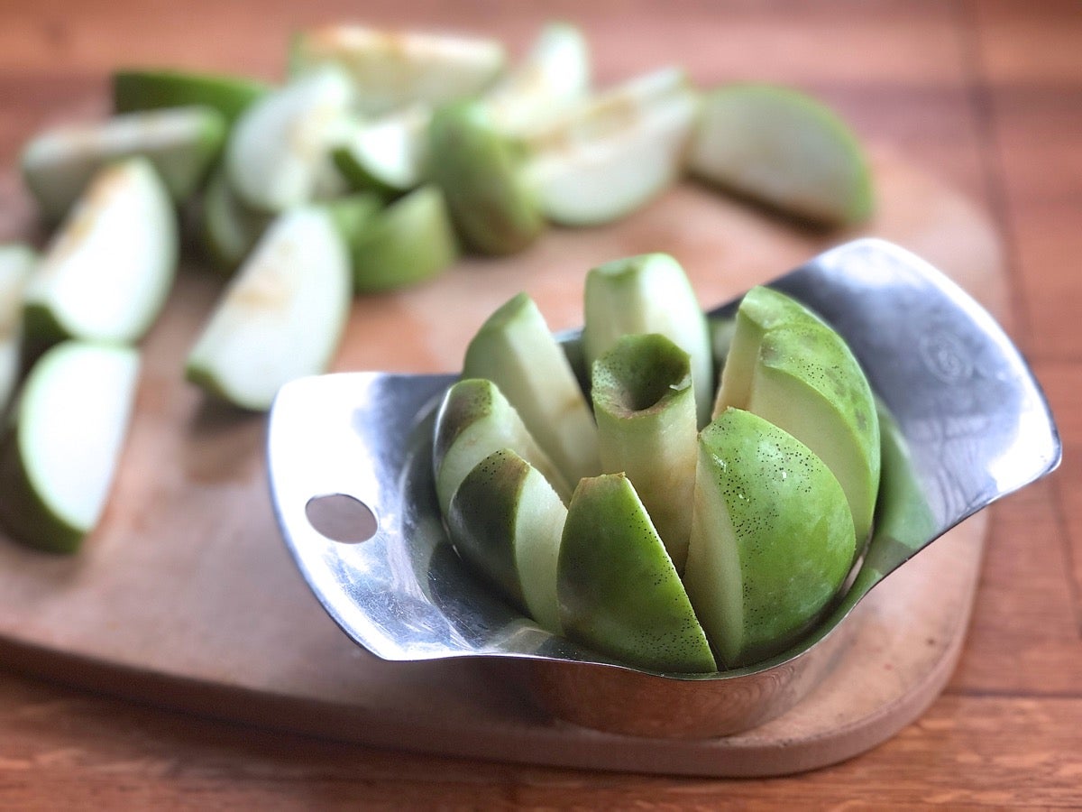 Green apples, one being cored with a stainless steel apple corer.