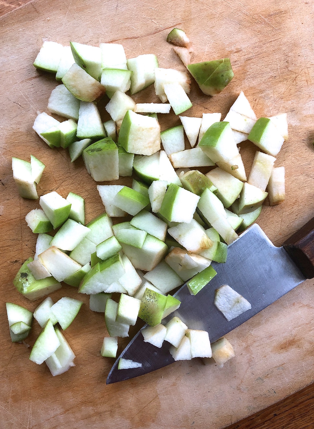 Unpeeled green apples chopped on a cutting board with a chef's knife.