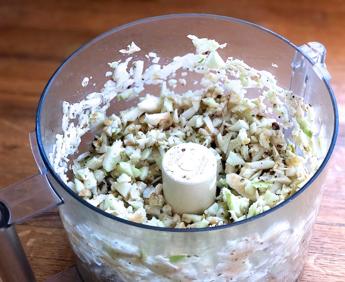 Apples and toasted walnuts in the bowl of a food processor, chopped.