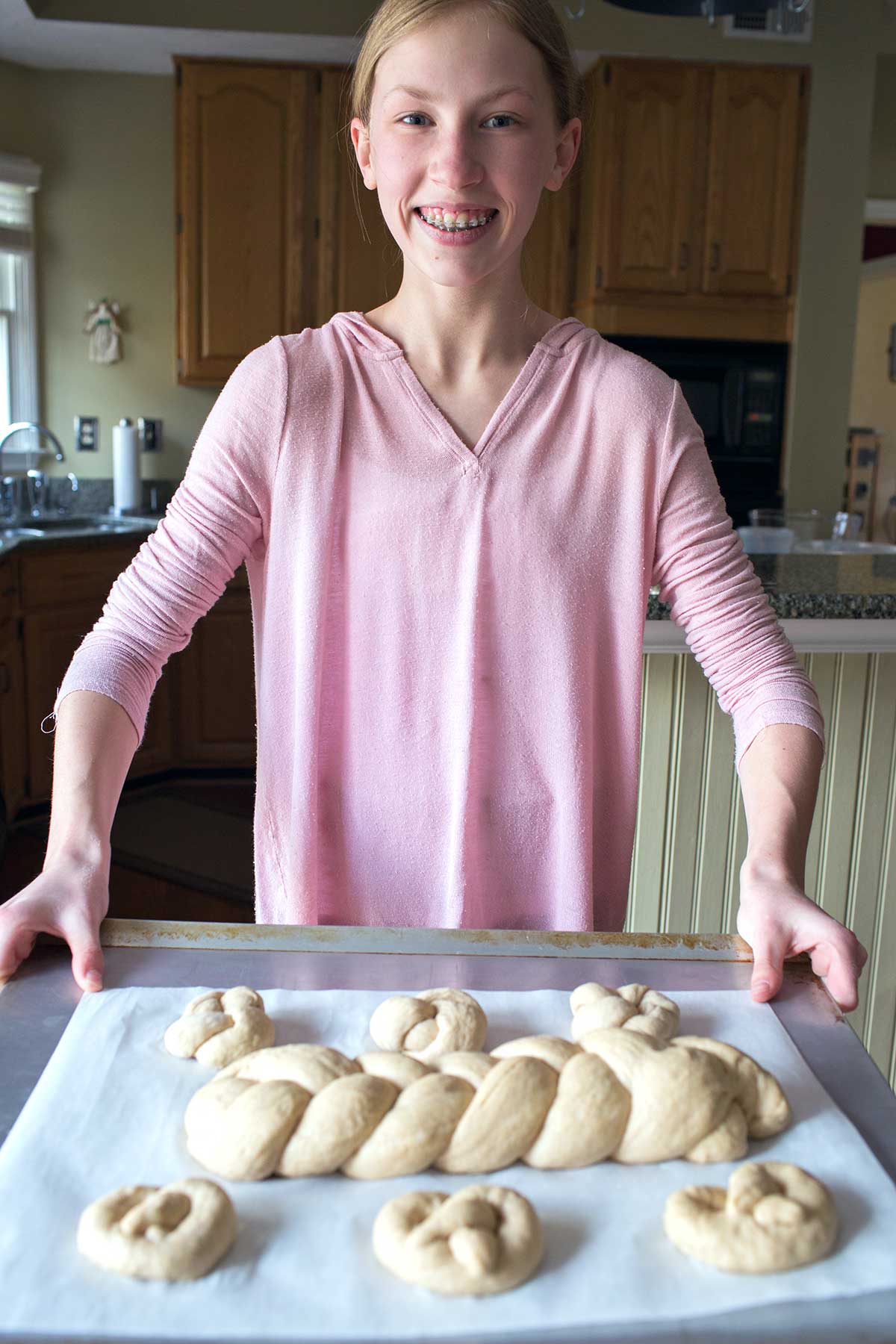 An older baker holding a tray of shaped loaves of challah