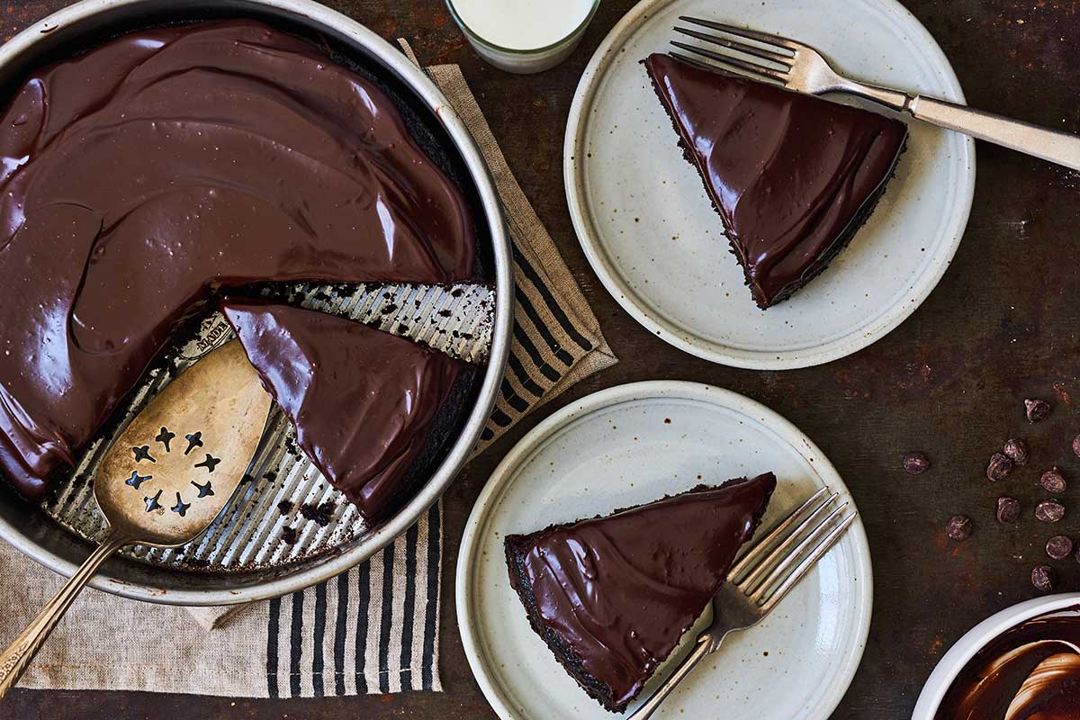 King Arthur's Original Cake Pan Cake in a round cake pan topped with chocolate ganache and a few slices on plates