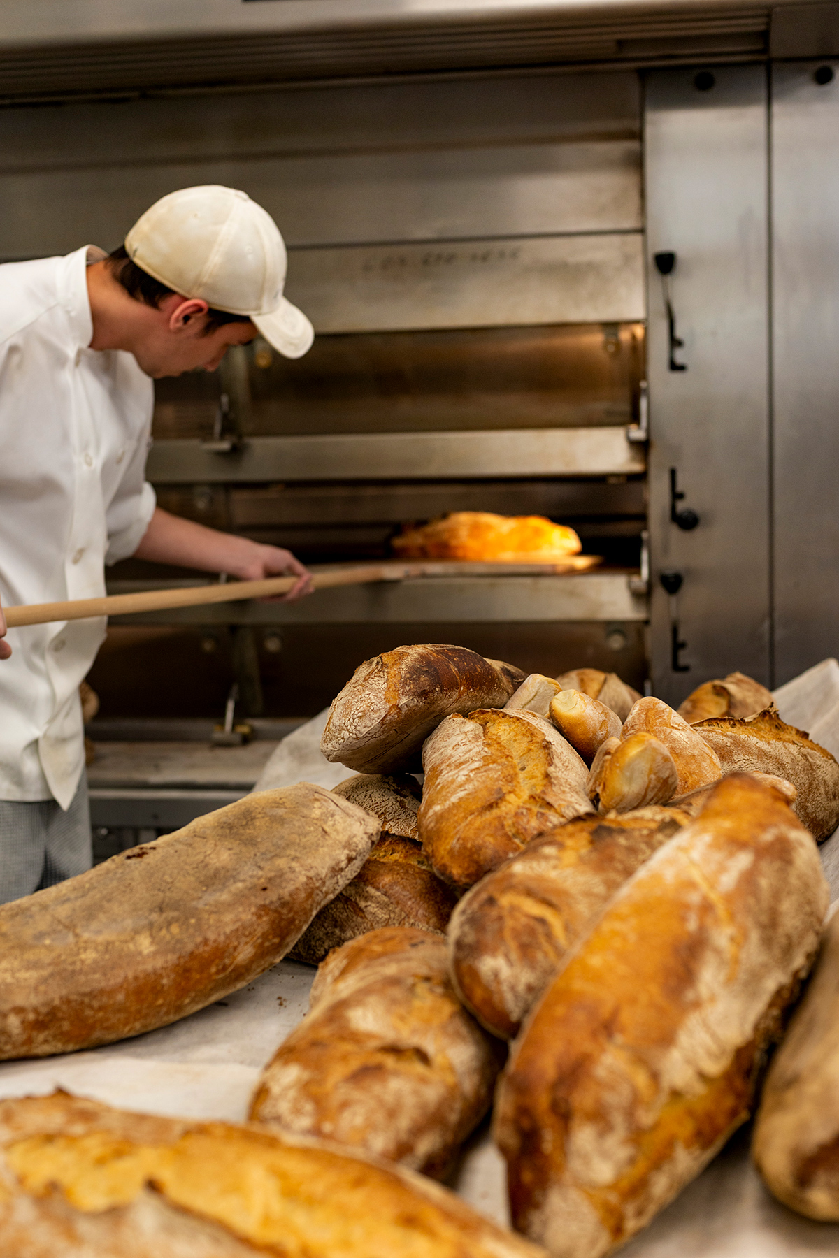 Baker pulling warm loaves of bread from the oven