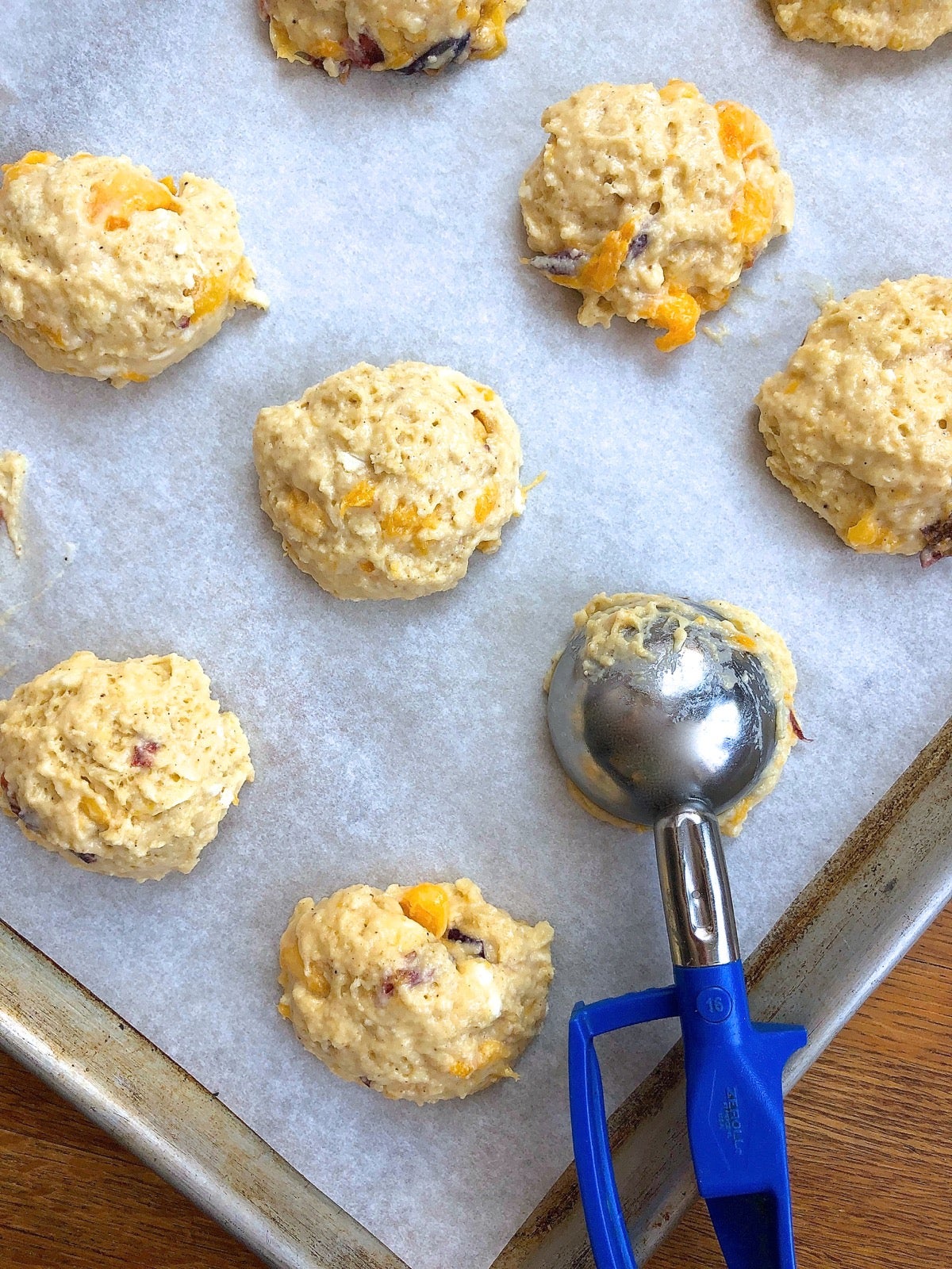 Peach scone dough dropped in rounds onto a parchment-lined baking sheet, ready to go into the oven.