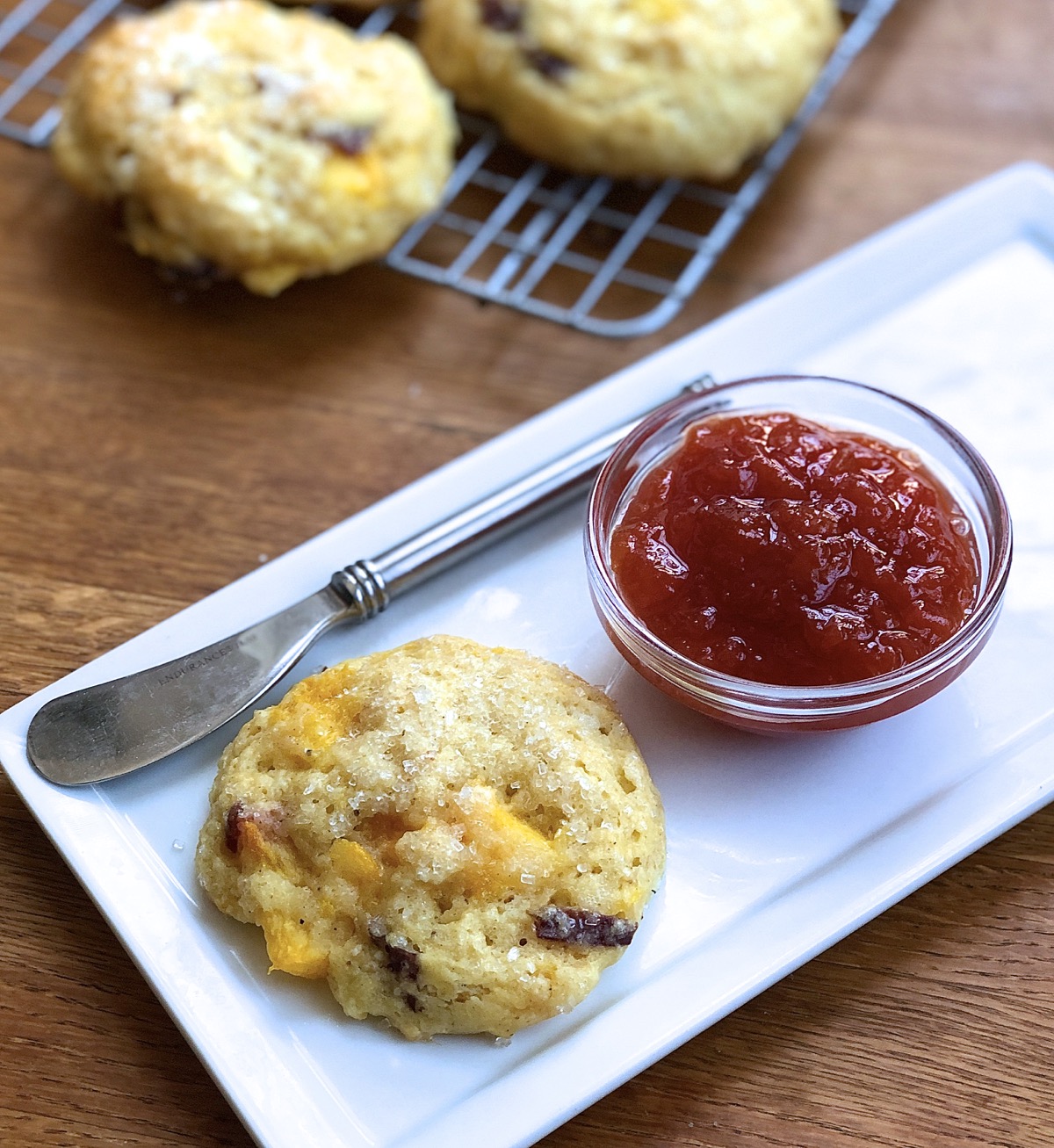 A peach scone on a plate with a butter knife and bowl of peach preserves, ready to enjoy.