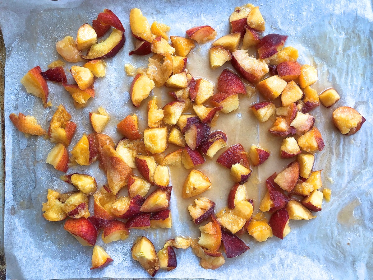 Diced unpeeled peaches on a parchment-lined baking sheet, ready to be oven-roasted.