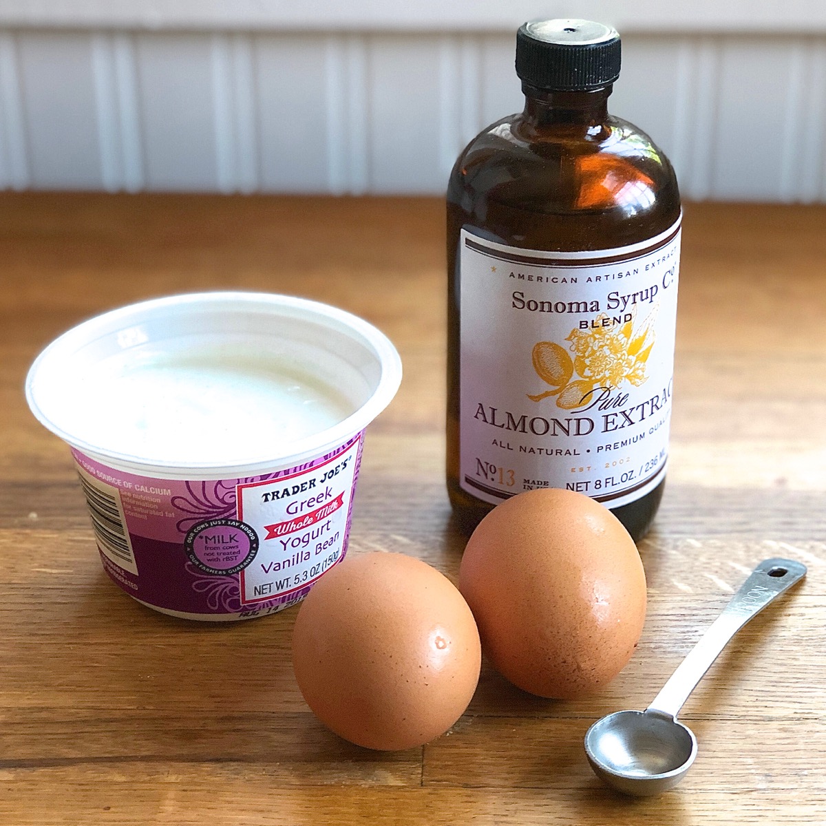 The liquid ingredients for peach scones: vanilla Greek yogurt, 2 large eggs, and a bottle of almond extract