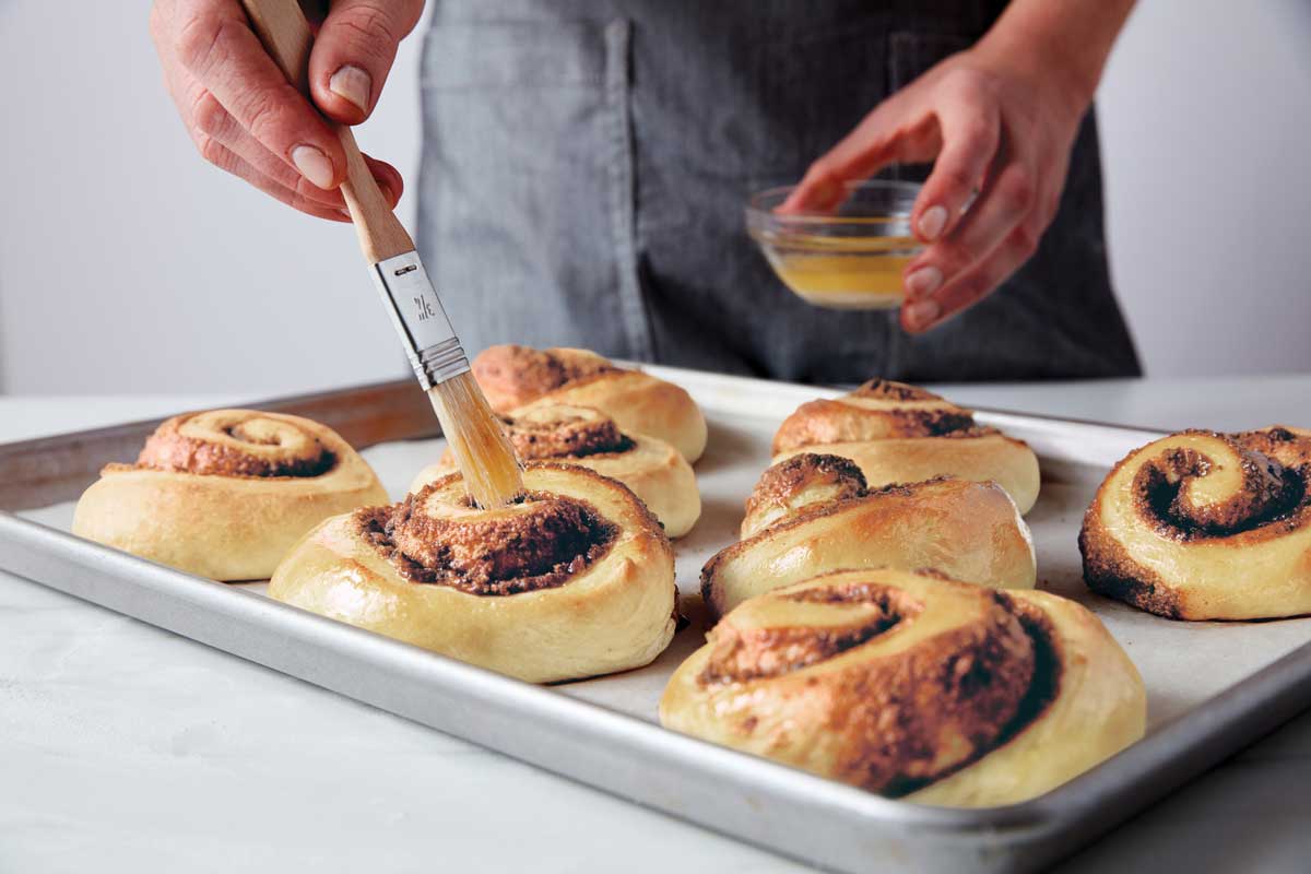 Just-baked cinnamon rolls being brushed with melted butter.