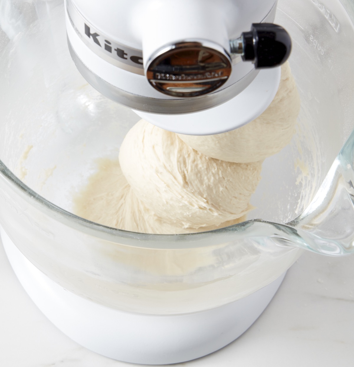 Cinnamon roll dough in the bowl of a stand mixer being kneaded, sticking to the bottom of the bowl.