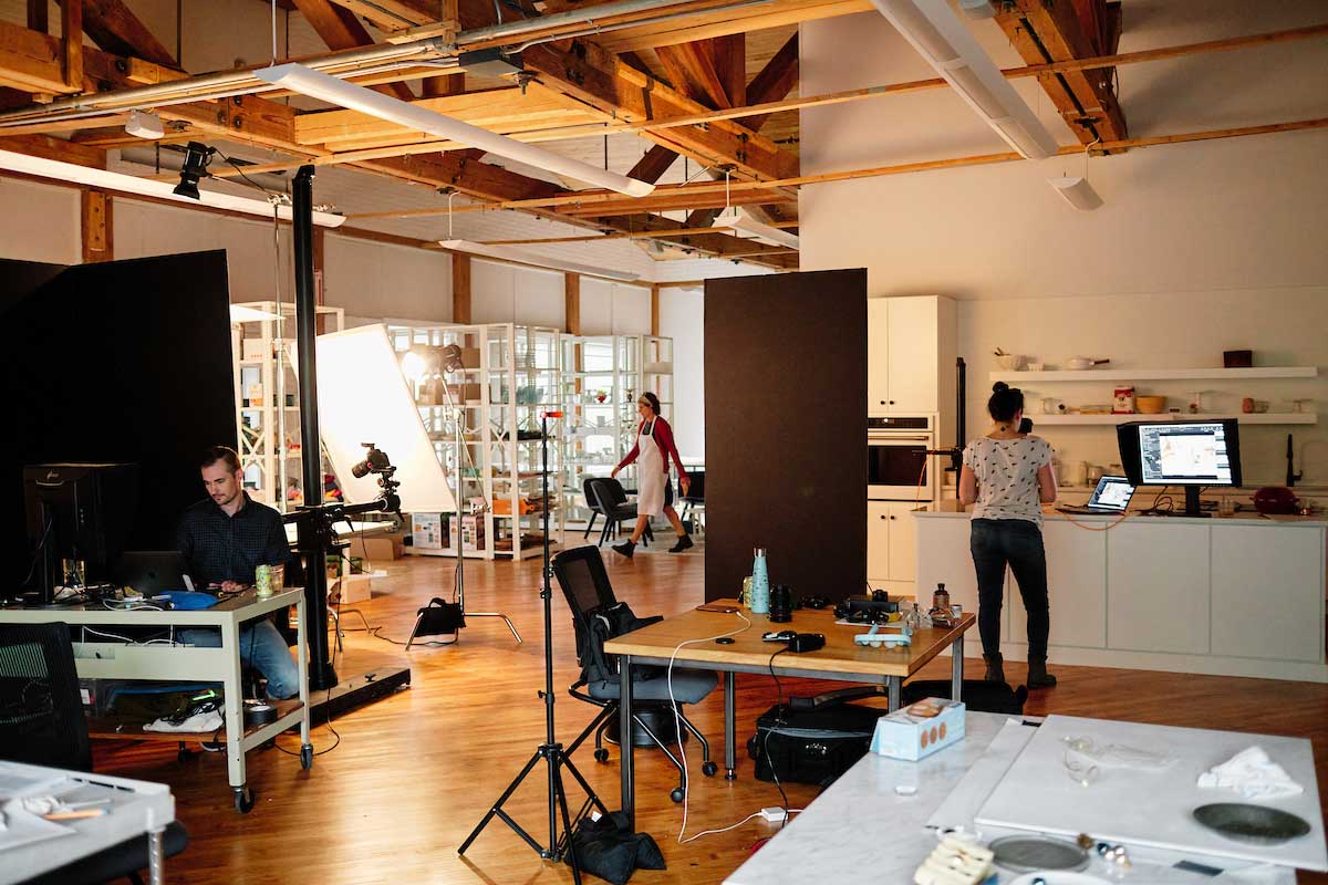 Interior of photo studio, showing photography kitchen, prop shelving, and open space with equipment and tables