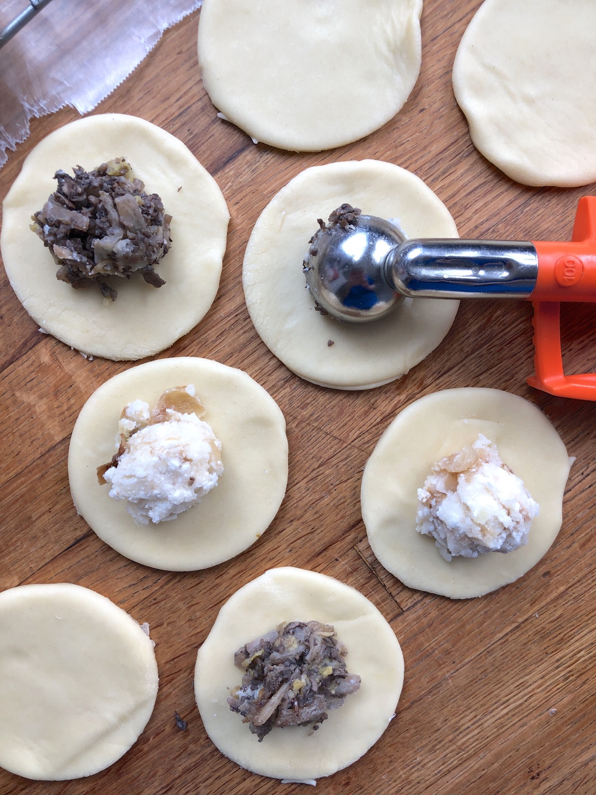 Filling being scooped onto rounds of pierogi dough using a teaspoon cookie scoop.