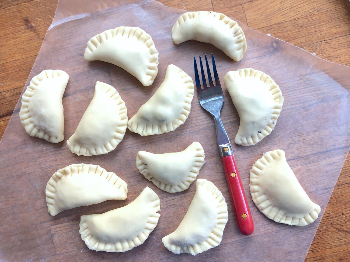 Shaped, filled, and sealed pierogi on a sheet of waxed paper, ready to cook.