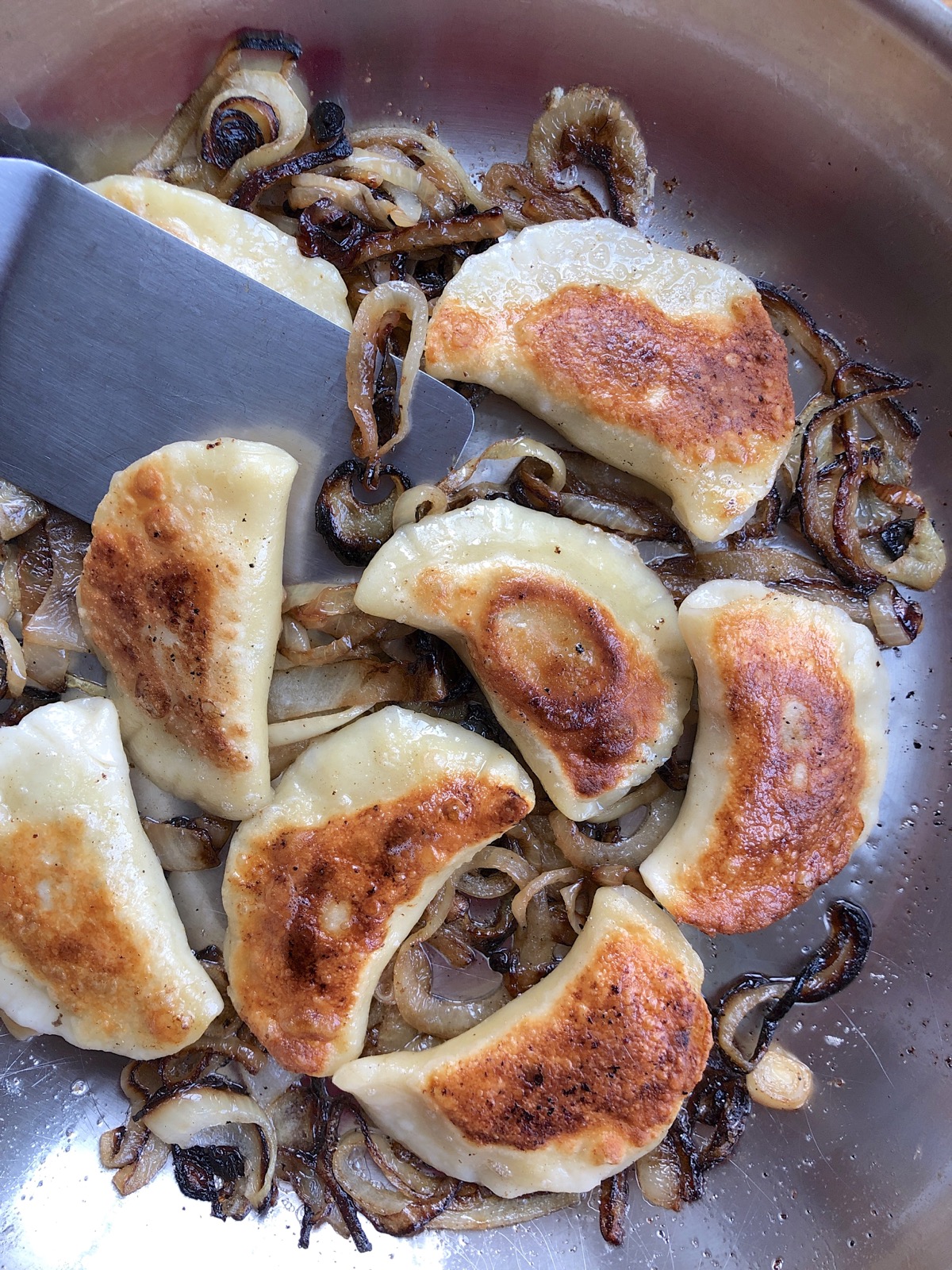 Browned pierogi cooking in a sauté pan surrounded by caramelized onions.