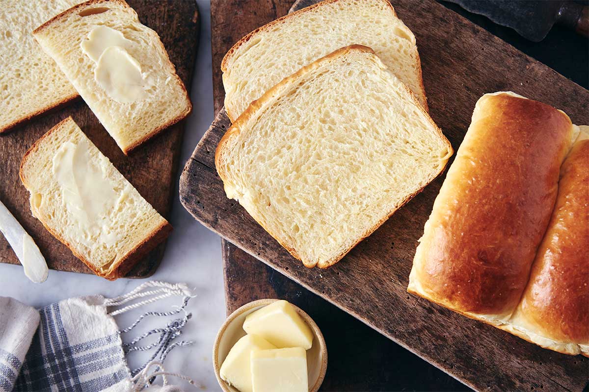 A loaf of Japanese Milk Bread cut into slices on a bread board