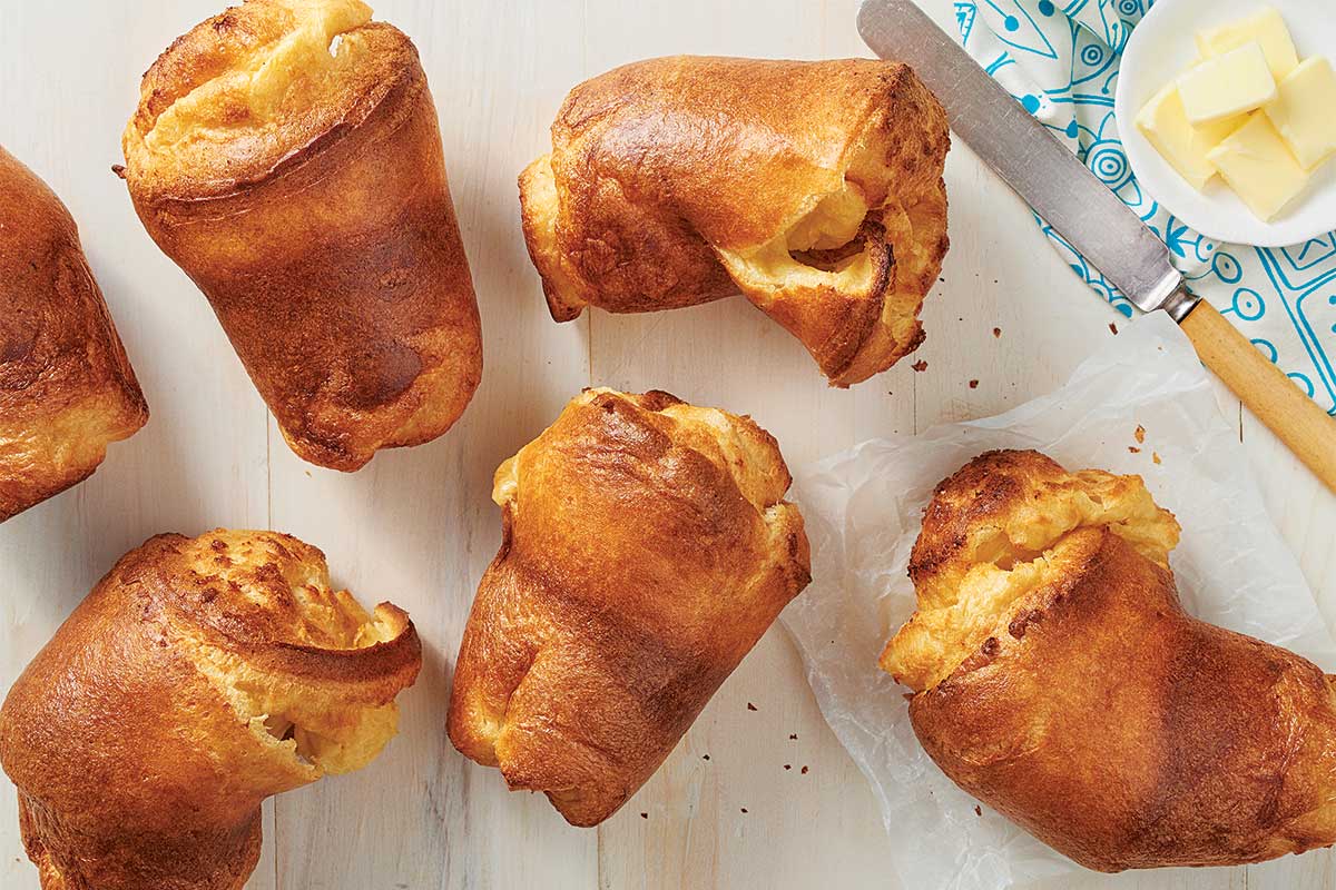 A half dozen golden brown popovers on a kitchen table