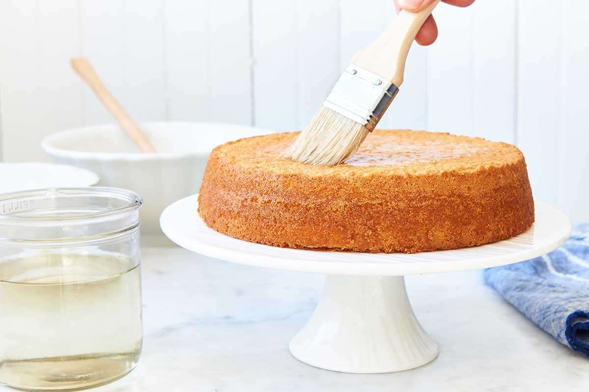 A yellow cake being brushed with simple syrup