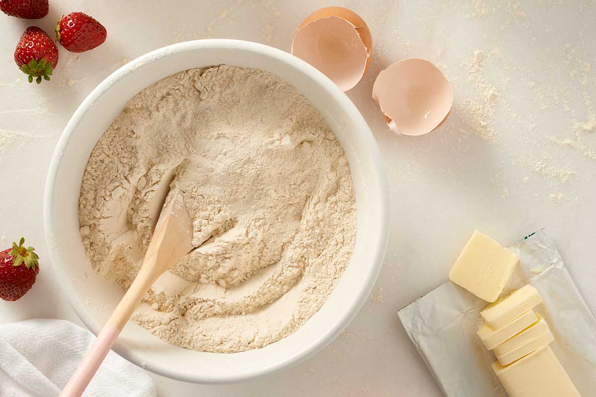 A bowl of dry ingredients next to eggs and butter