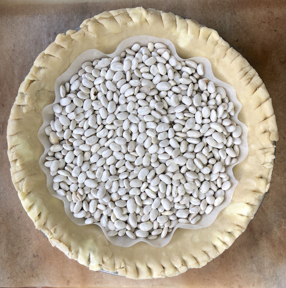 Unbaked pie crust lined with parchment and partially filled with dry beans, to weigh it down as it prebakes.