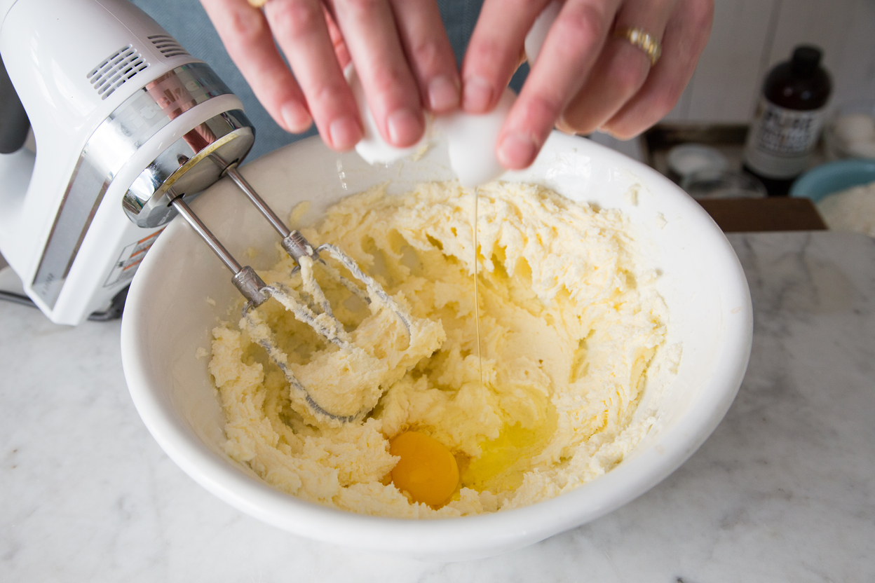 Cracking egg into bowl of creamed butter and sugar