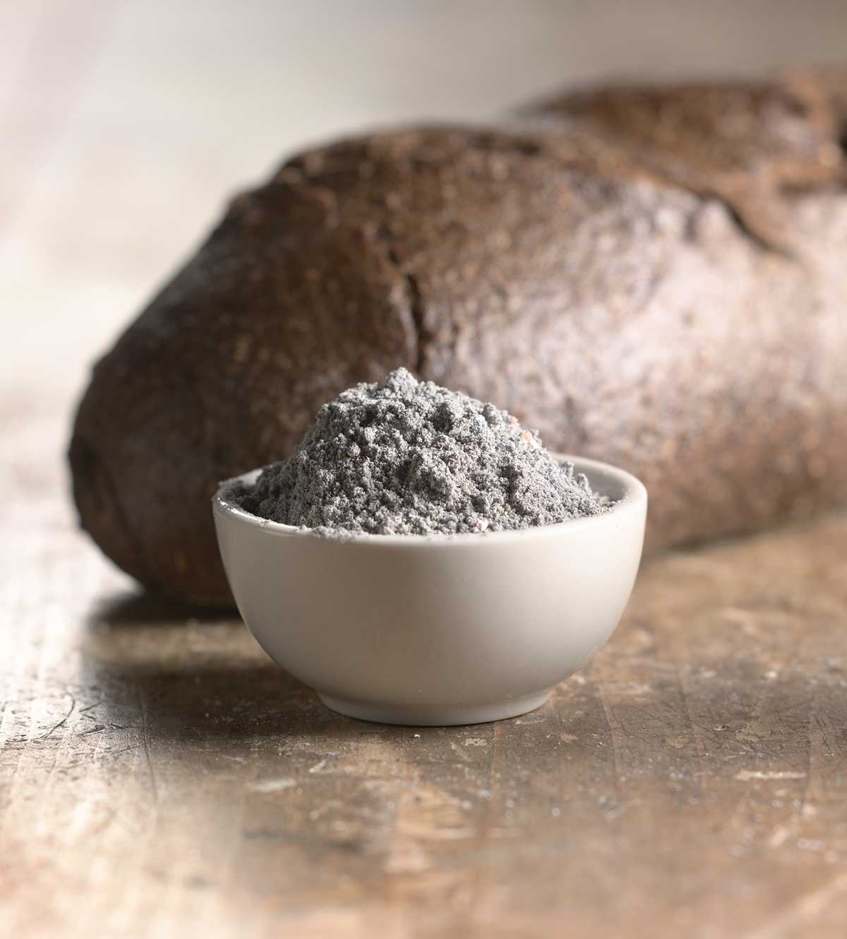 Bowl of pumpernickel flour, with dark loaf of bread in the background