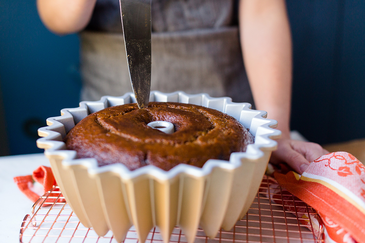 A baker testing a pumpkin Bundt cake for doneness with a paring knife