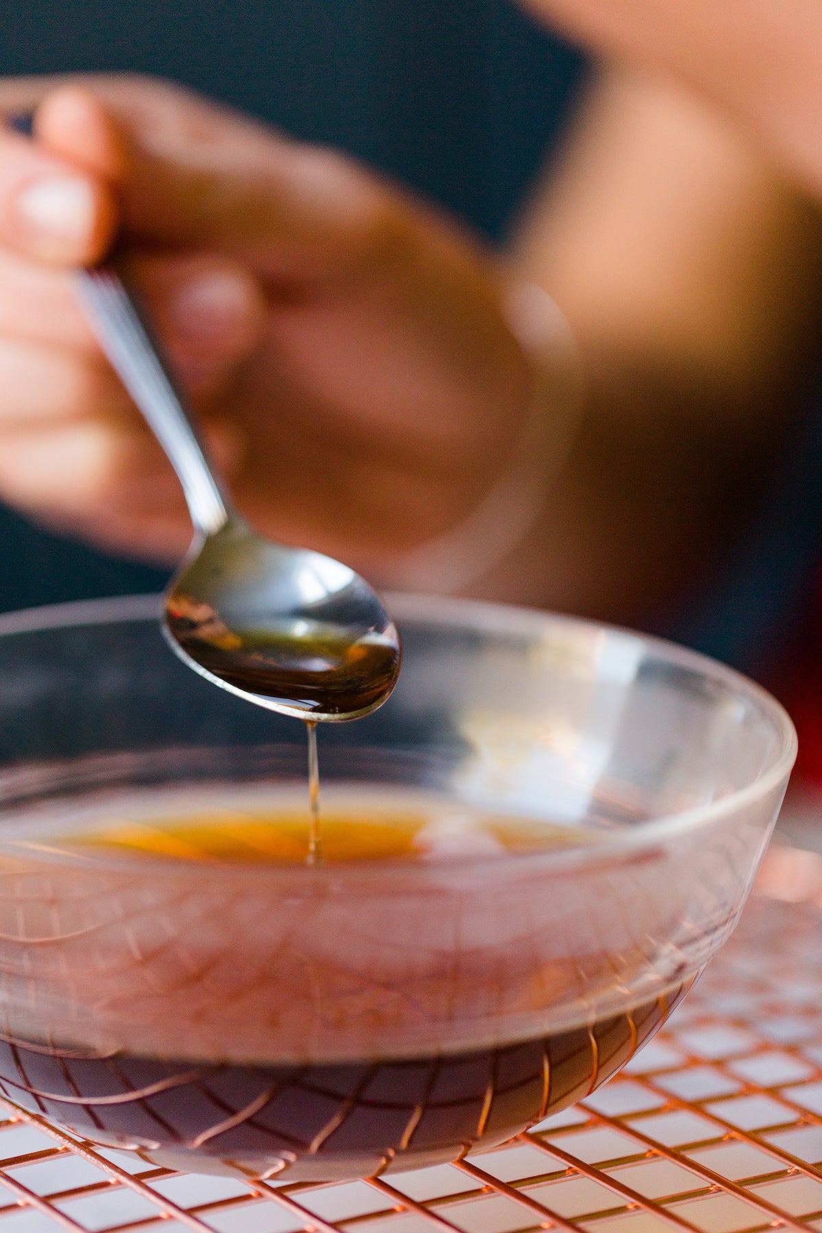 A person holding a spoonful of coffee-rum glaze, ready to be brushed on the Bundt cake