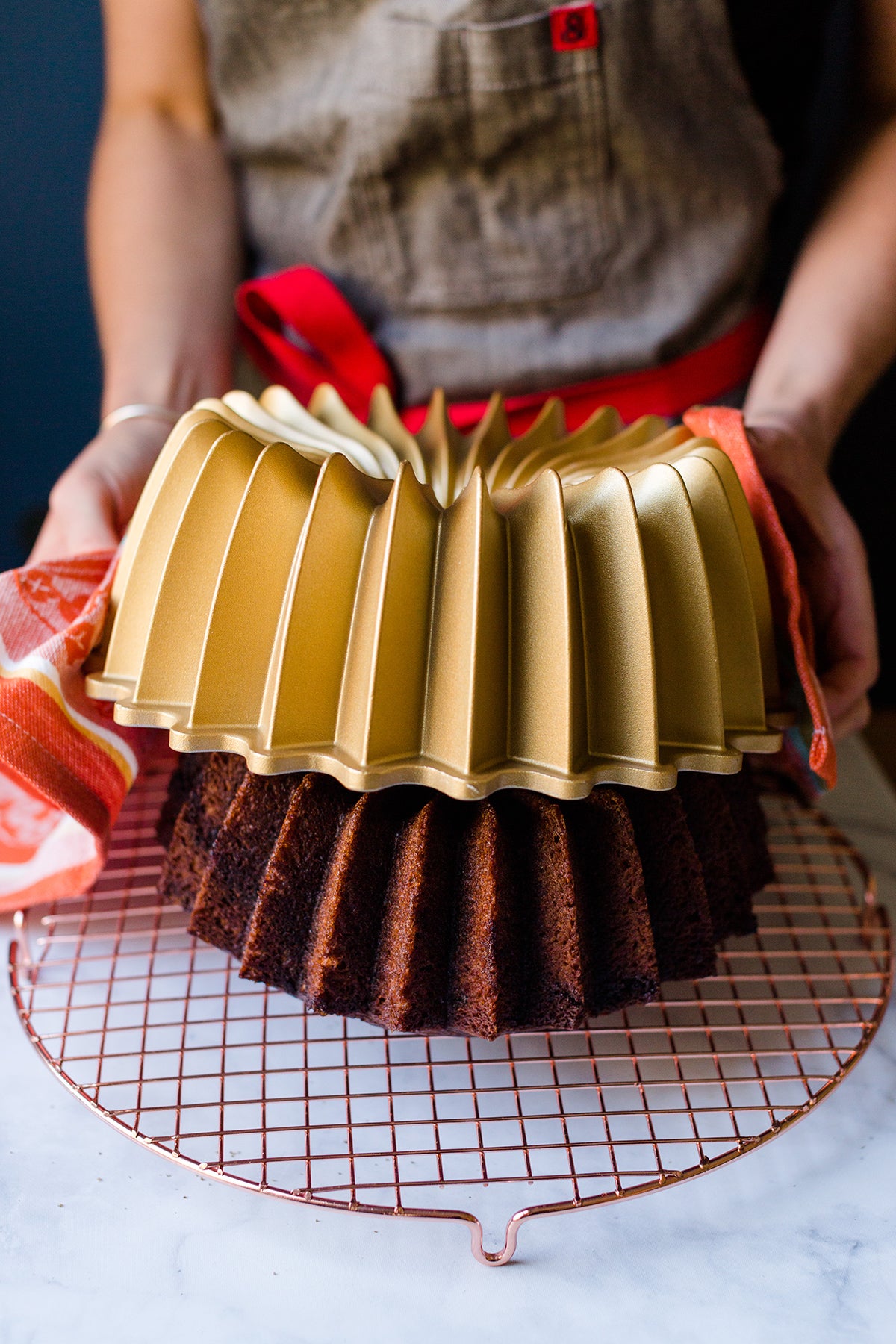 A baker lifting up a Bundt pan to reveal a pumpkin-espresso cake