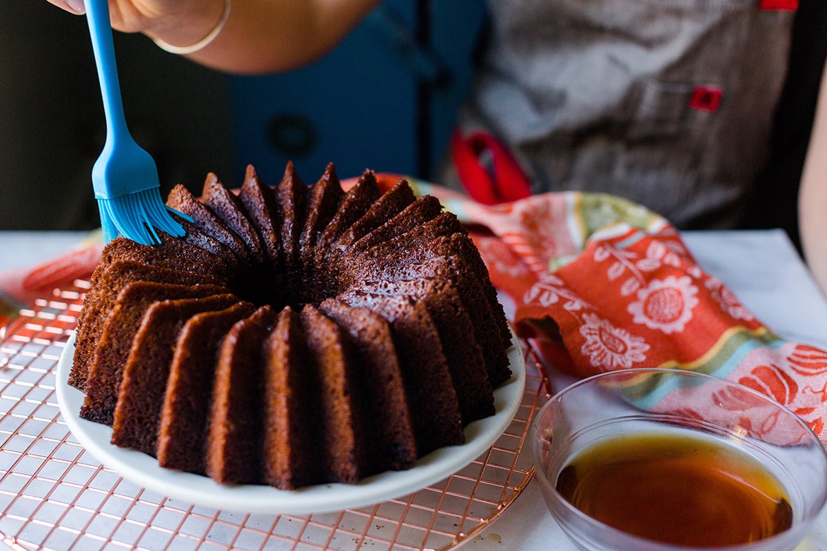 A baker brushing coffee-rum glaze onto a pumpkin Bundt cake