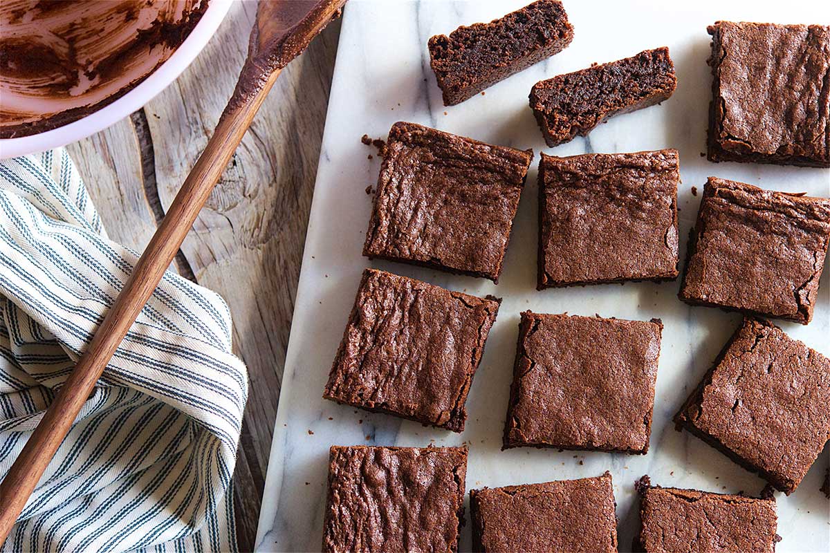 A batch of brownies cut into squares next to a mixing bowl of brownie batter