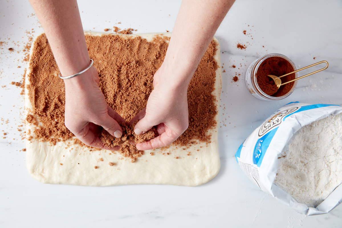 A baker spreading cinnamon filling on rolled out dough